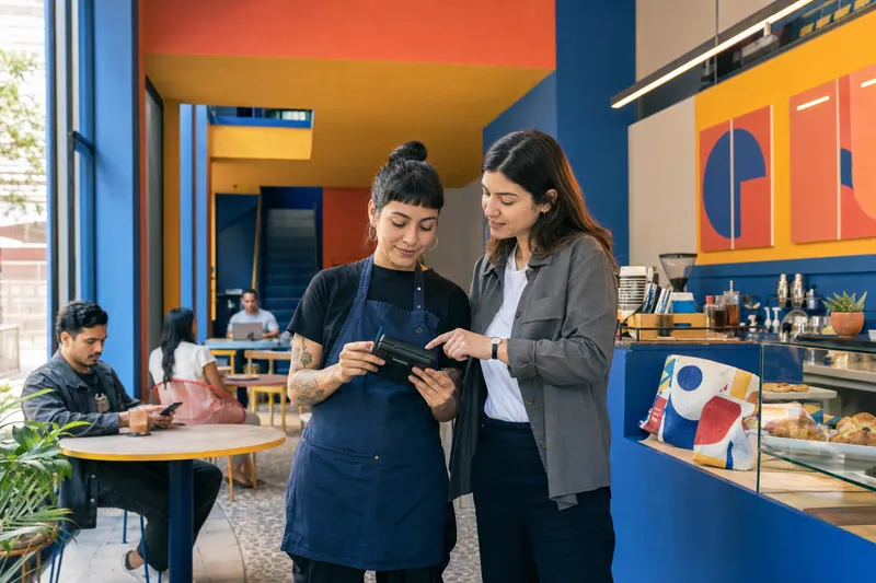 Dos personas revisan una tableta junto a la barra de una cafetería con muros de colores