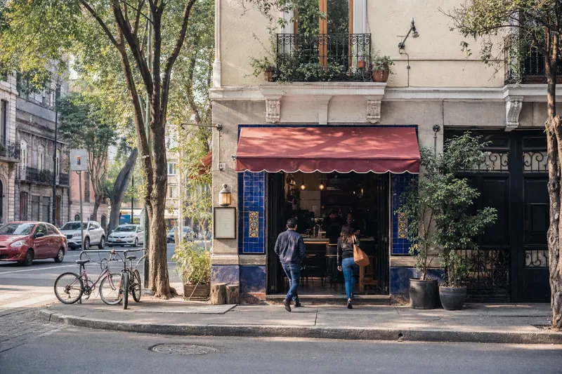 Dos personas entran a una cafetería en una esquina arbolada