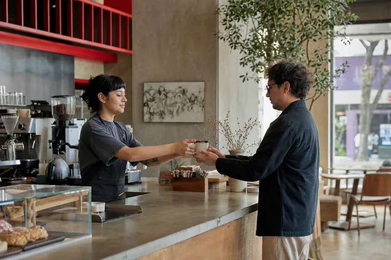 Una barista entrega una bebida a un cliente en el mostrador de una cafetería